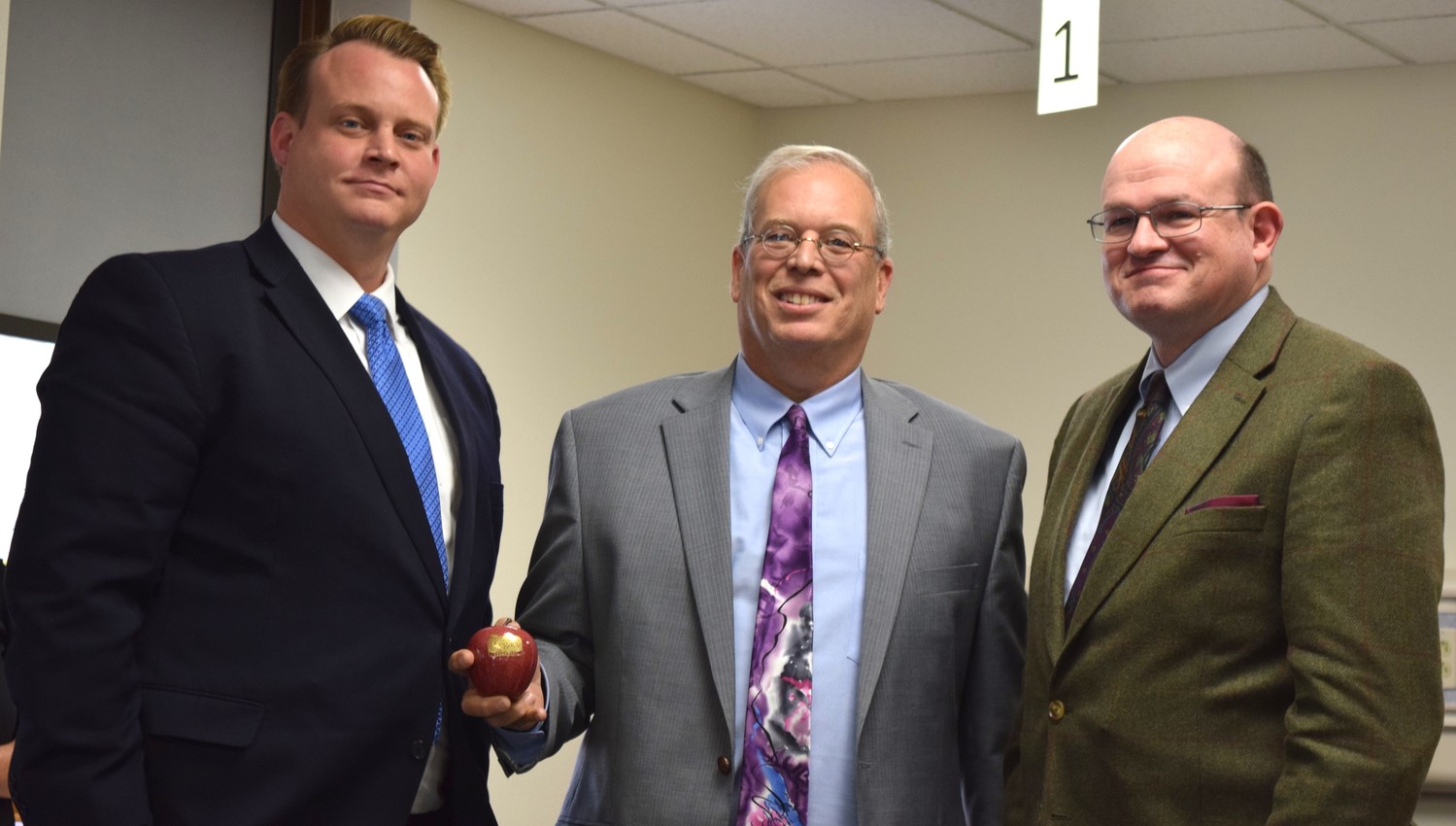 Skaggs Foundation grant committee member Matt Trokey, center, awards a ceremonial apple representing grant funding to Ozarks Technical Community College Table Rock Dean Robert Griffith, left, and Chancellor Hal Higdon.