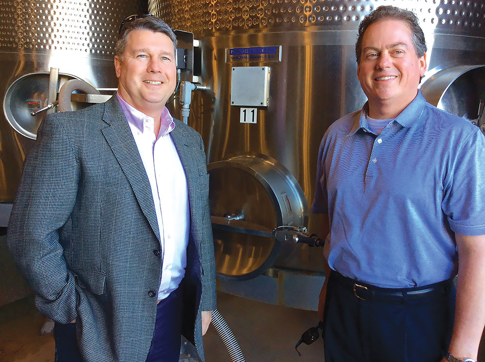 Business Class co-hosts John Wanamaker, left, and Randell Wallace are pictured next to a Paul Mueller Co. tank at a Napa Valley winery in 2015.SBJ photo by JENNIFER JACKSON