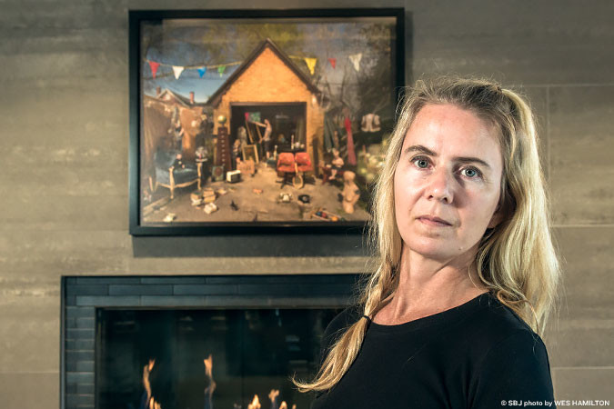 Photographer Julie Blackmon stands in front of a print of her 2013 work “Garage Sale,” which hangs at the downtown Hotel Vandivort. Her work has been featured in international magazines, including Time.