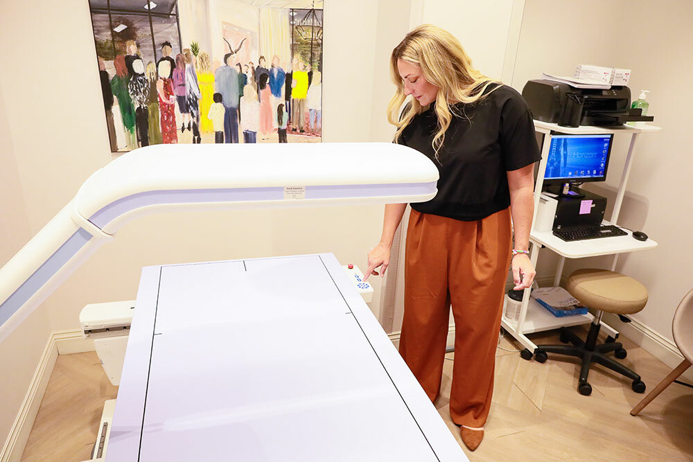 Action Painting: At The Breast Center, as the office is more familiarly known, bone mineral density scanning is offered in addition to mammography services. Dr. Amanda Lackey stands before a live-action painting of her friends and family executed by an artist at the center’s opening.