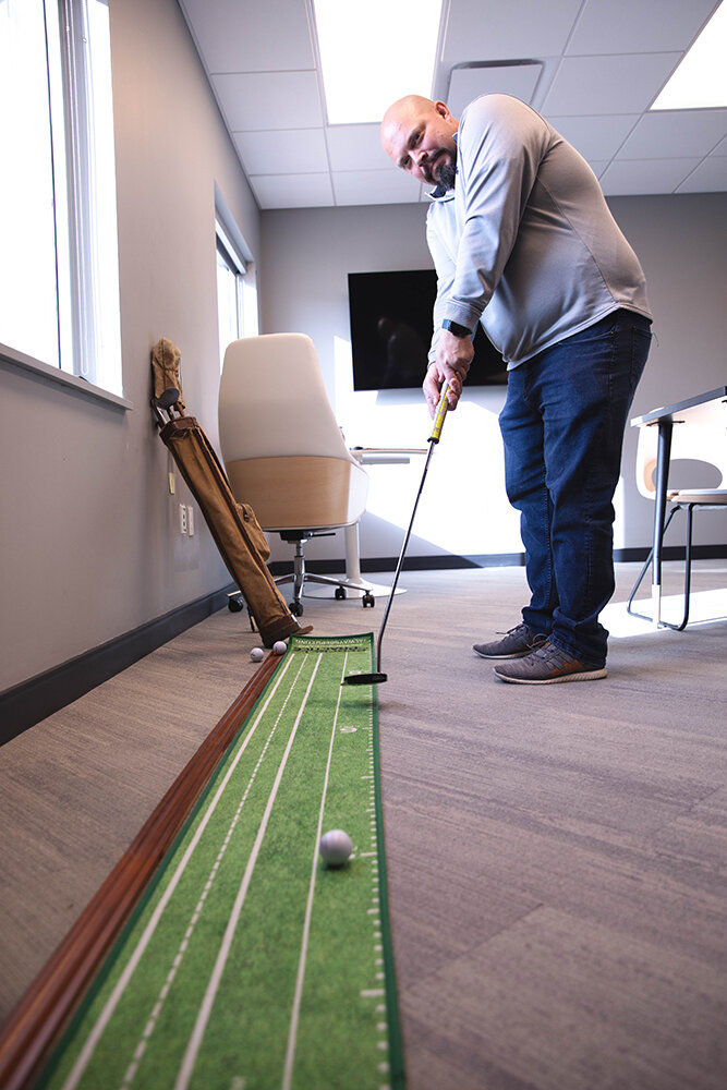 In the Hole: Chief Operating Officer Steve Bishop takes aim on the putting green in his office that is adjacent to the center’s lobby.
