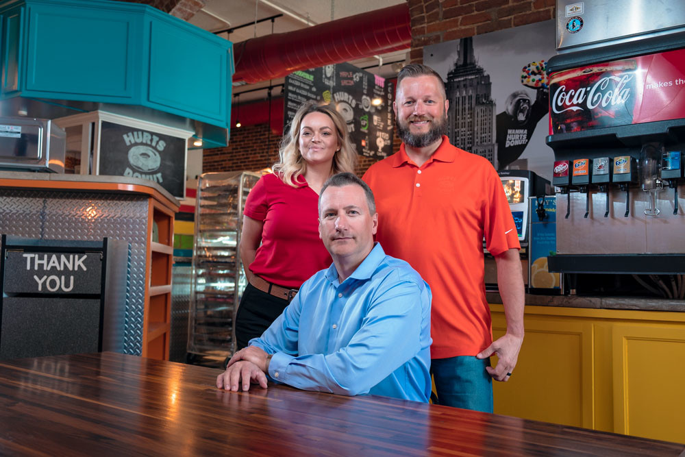 The leadership team at Hurts Donut Co., — Kas Clegg, left, Scott Bussard and Tim Clegg — have 18 shops open, with more soon to follow.