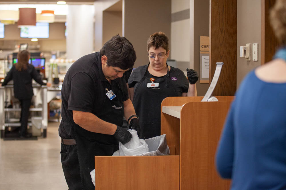 Developmental Center of the Ozarks employees Donnie Curran and Olive Henopp team up to change out trash receptacles in the Cox South Hospital cafeteria.