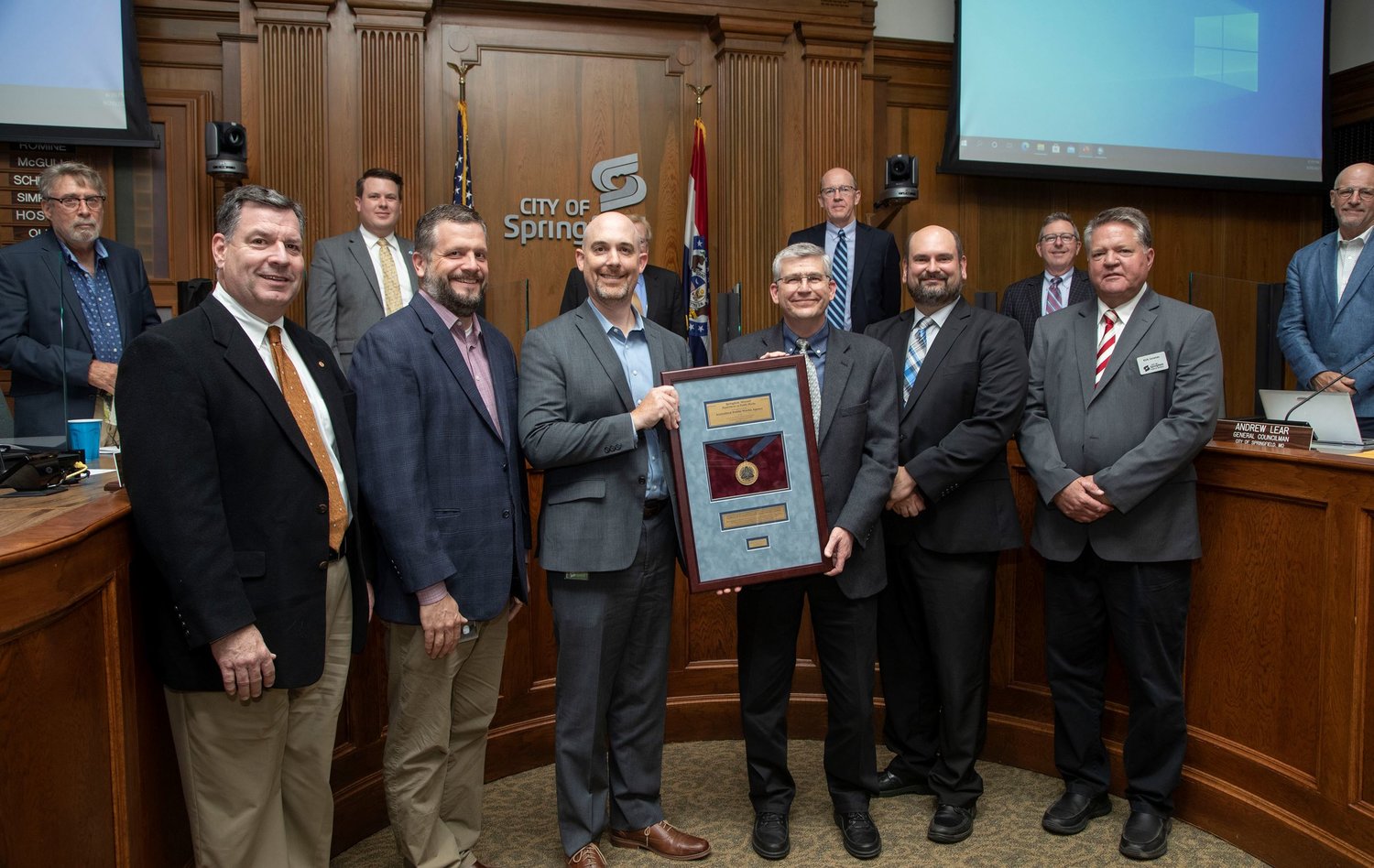 Leaders of the city's Public Works and Environmental Services departments display their reaccreditation plaque in council chambers.