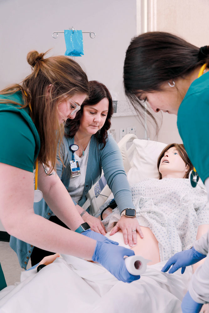CONTROLLED ENVIRONMENT: Cox College nursing students Amanda Daves and Andrea Camargo practice applying a dressing to a mannequin with Tina Toles, simulation coordinator.