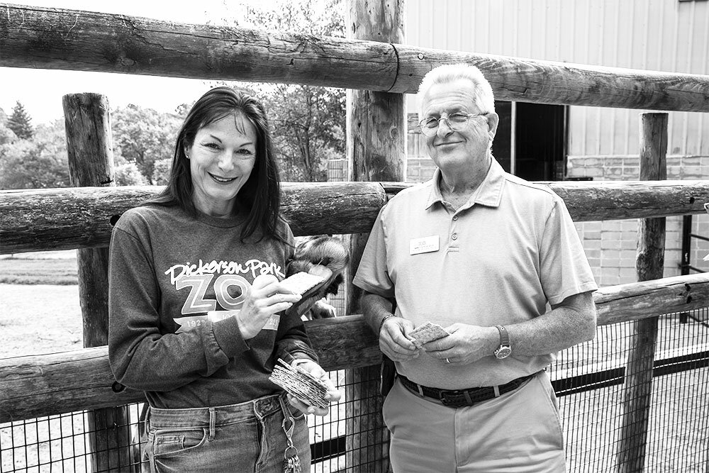 SNACK TIME: A sneaky giraffe takes a treat out of the hand of Joey Powell, public relations and marketing director for Dickerson Park Zoo and Friends at the Zoo, while longtime zoo Director Mike Crocker looks on.